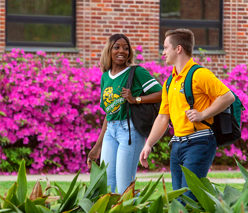 Two Students Walking On Campus in Front of Azaleas