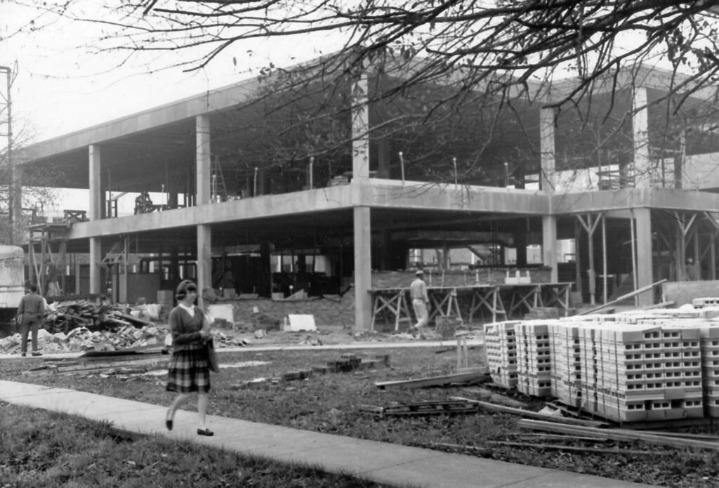 A female student walks past a building under construction on campus in the 1960s.