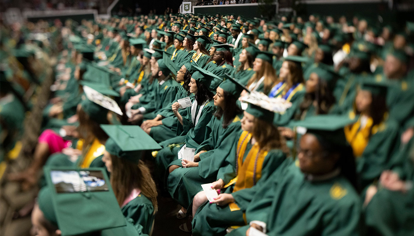 photo of graduates dressed in green cap and gowns sitting in rows